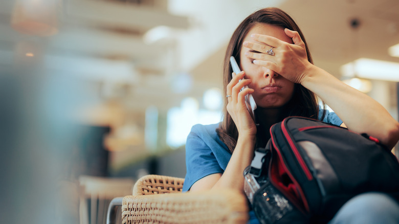 Stressed traveler speaking on her cellphone in the airport feeling overwhelmed