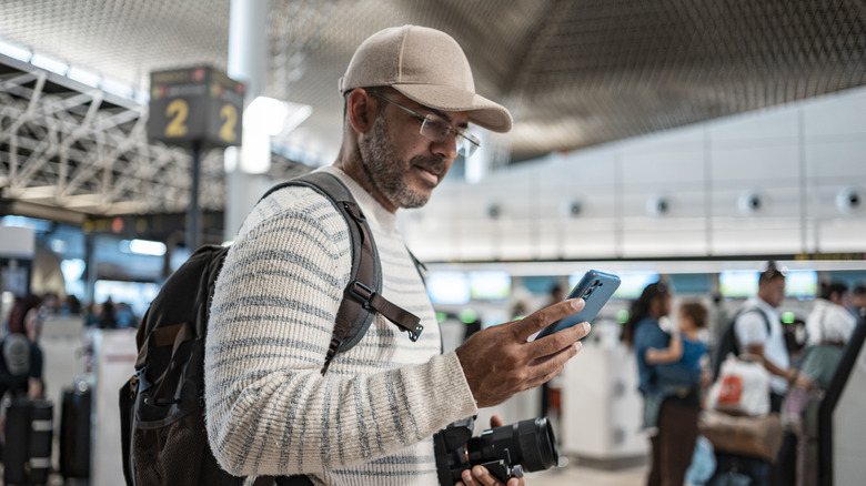 Middle aged man wearing a ball cap using his cell phone at the airport getting ready for a trip