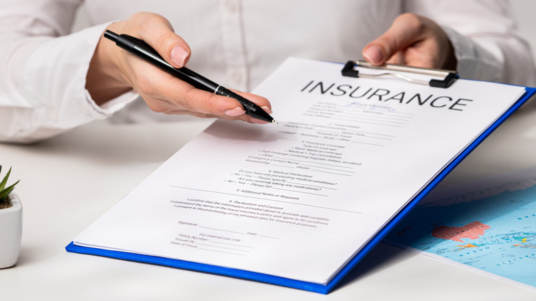 Close-up of a woman's hand holding a travel insurance claim paper on a billboard with a world map underneath, indicating lots of manual work