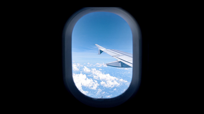 Airplane window showing blue, clear sky and beautiful clouds