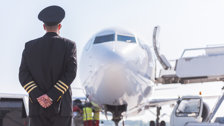 Pilot wearing uniform is standing outside and looking a at plane