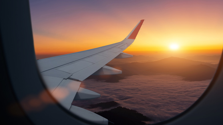 Airplane flying low over foggy mountains, view from plane window of plane wing and sunrise