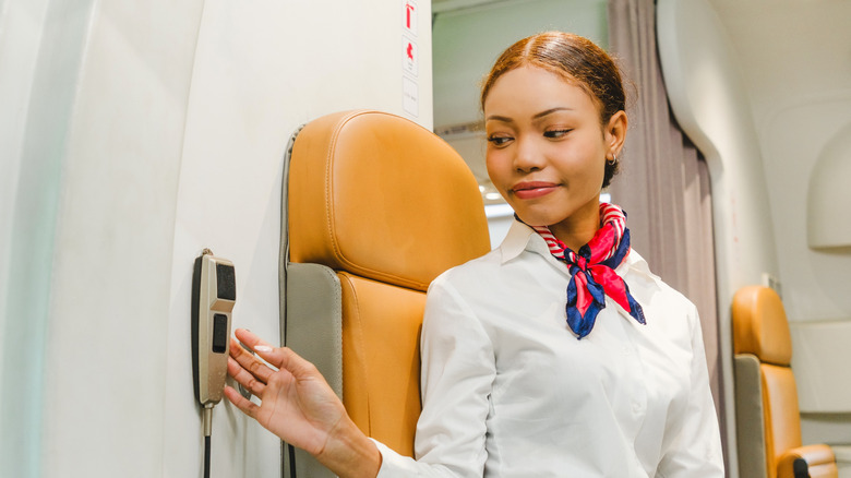 Flight attendant in uniform uses the cabin intercom inside an airplane