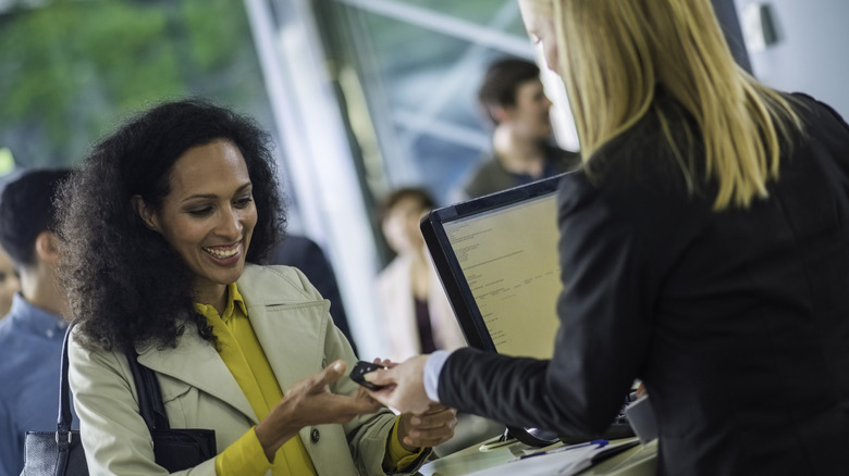 Two women on opposite sides of car rental counter, with the customer smiling as she is handed a rental car key