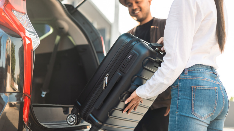 Happy couple loading a suitcase in the back of a black hatchback SUV