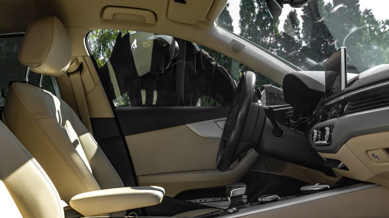 Masked thief looking in the window of a sedan with a tan leather interior
