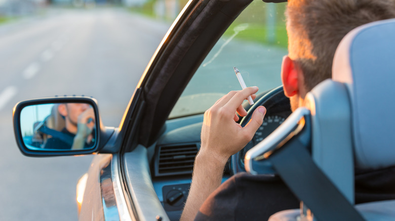 View from behind of a man with cigarette in the car, visible in side mirror with the window down
