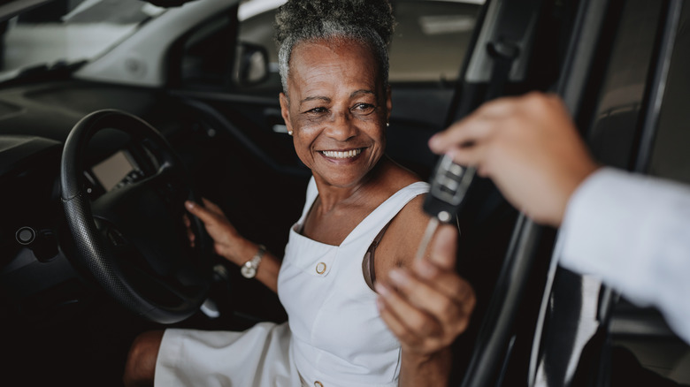 Senior African American woman being handed the key to a rental car with a black interior