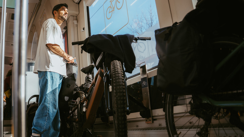 An artistic angle taken from the ground of a young man standing inside a train with his bicycle parked along the outer wall