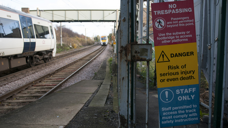 A danger and no trespassing sign are displayed beside rail tracks as an oncoming train approaches