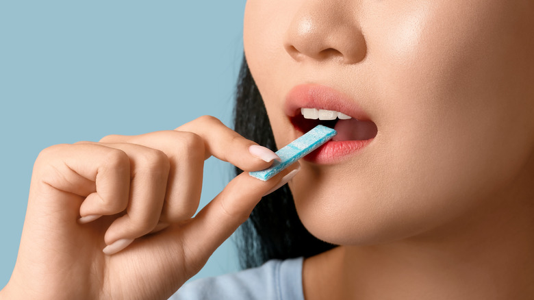 Pretty young Asian woman with open mouth holding chewing gum on blue background, closeup