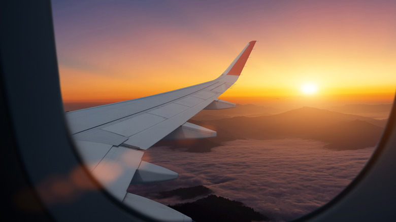 Airplane flying low over foggy mountains, view from plane window of plane wing and sky sunrise
