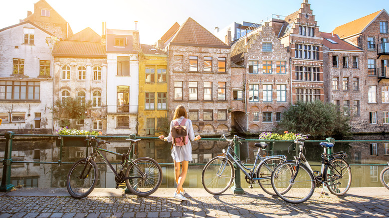 Sunrise view on the water channel with beautiful old buildings with woman standing near the bicycles in Gent city
