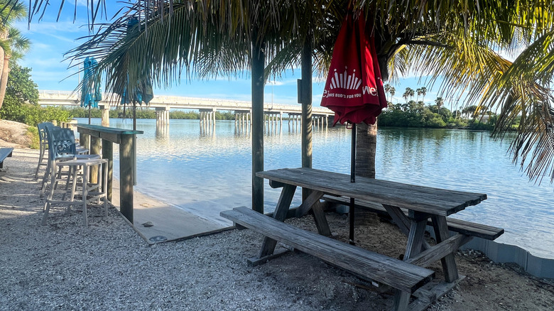 A picnic table with red umbrella by the water