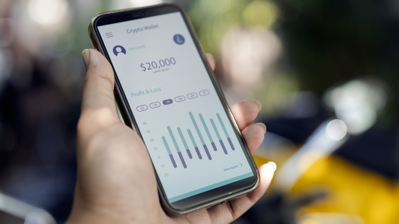 Close-up of a hand holding a phone that shows financial data on a crypto wallet app