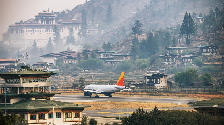 Plane on a runway, surrounded by mountains and houses, at Paro International Airport, Bhutan