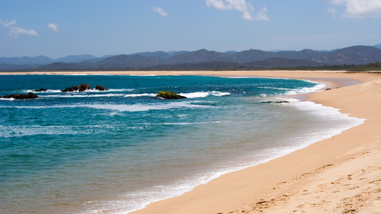 Golden sand and blue water with mountains in the distance on Mayto Beach, Mexico