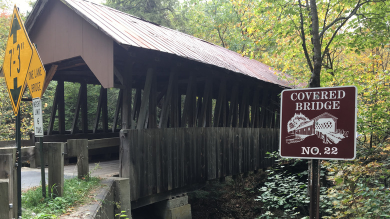 Covered bridge in Cornish surrounded by green trees.