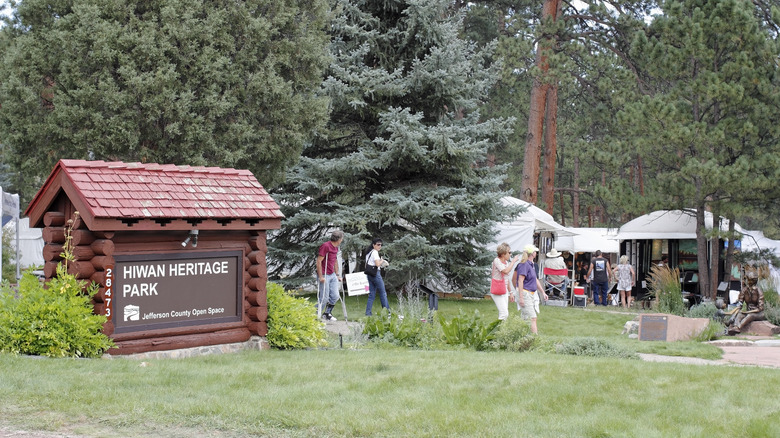 Sign for Hiwan Heritage Park with trees and people in the background