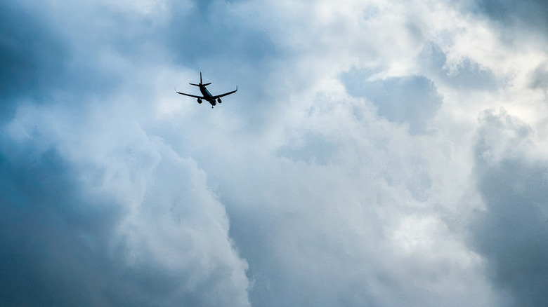Silhouette of a plane flying high into dark, stormy clouds