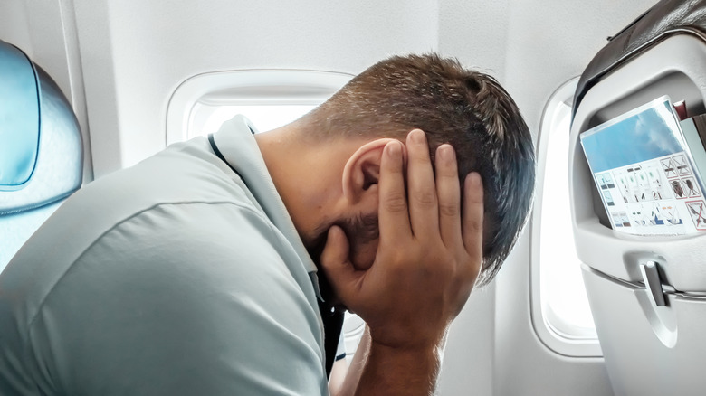 Man on a plane puts his head in his hands near the window