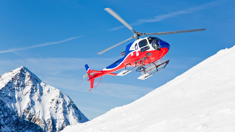 A helicopter flying parallel to a snowy mountain slope