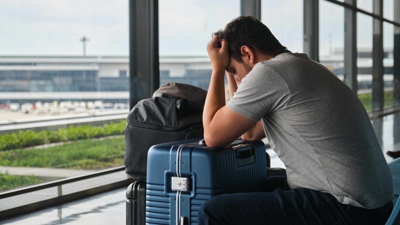 Man sitting in airport with his head in his hands and leaning on his luggage in front of him