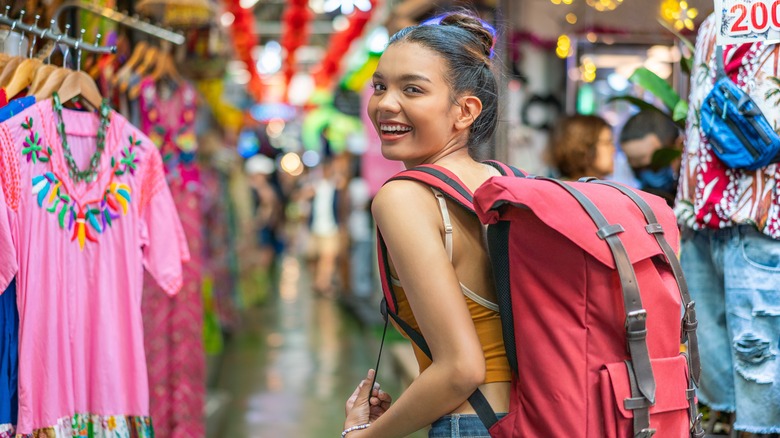 Woman wearing backpack looking behind her smiling in outdoor market