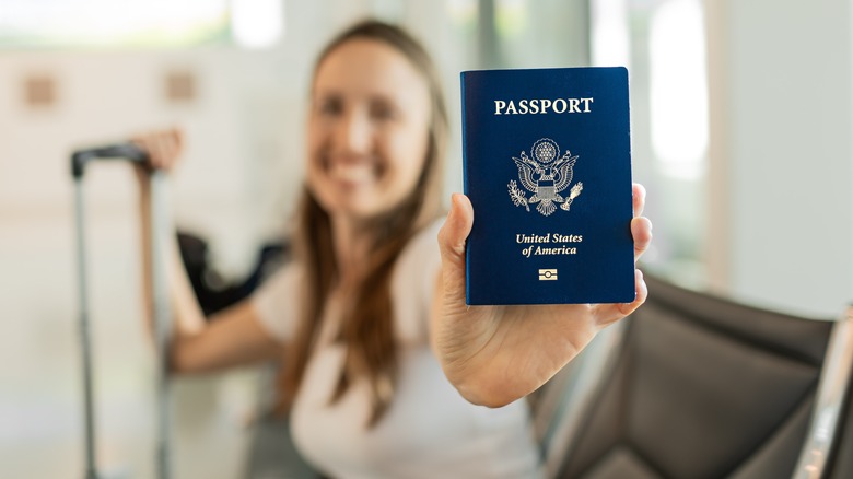 Blurry image of woman smiling with luggage holding American passport in front of her