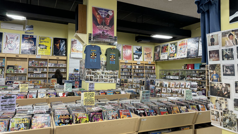 Interior of Eide's Entertainment, with wooden racks of comic books in the foreground, a yellow column with a Star Trek Poster and two t-shirts hanging from it, and shelf-lined yellow walsl in the background