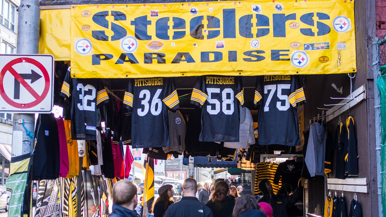 Yellow sign reading "Steelers Paradise" over steelers jerseys and attire, with a crowd of people walking down the sidewalk under it