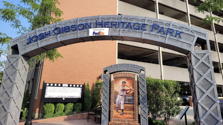 Gray arch reading "Josh Gibson Heritage Park" in front of a red brick wall, over a painting of Josh Gibson surrounded by trees and benches