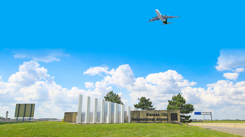 plane flying in blue sky over Kansas City International Airport sign