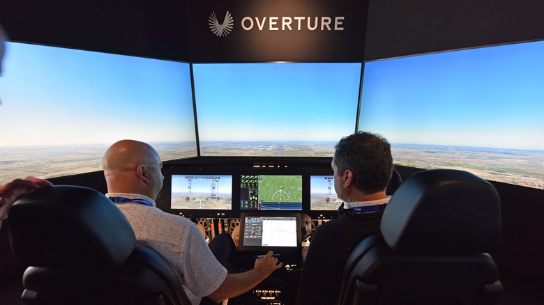Two men sitting in a flight simulator for the Boom Overture supersonic jet.