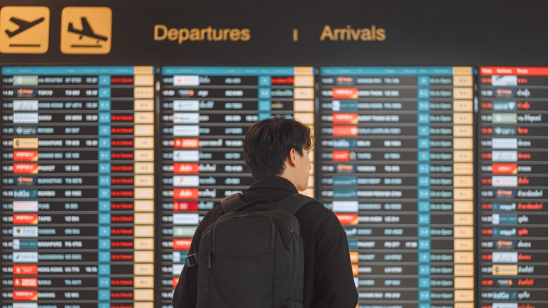 A man checks his flight details on an airport information screen