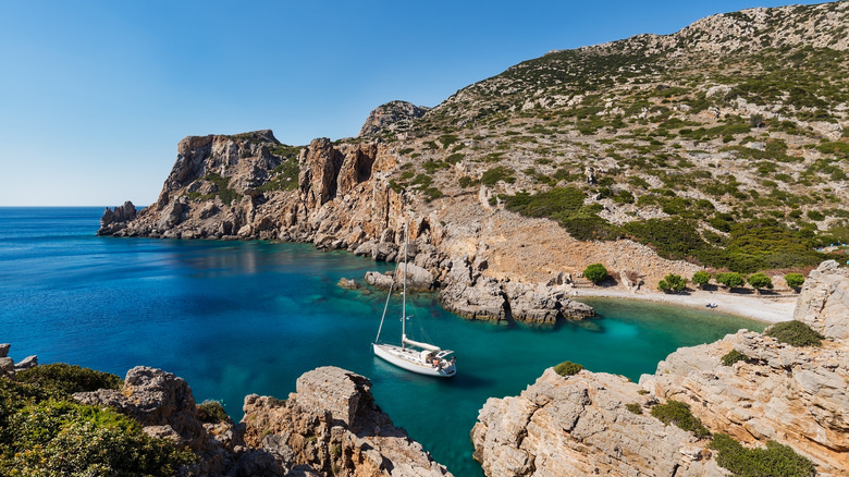 Sailboat anchored in front of a rocky bay with crystal-clear turquoise waters, Saria Island