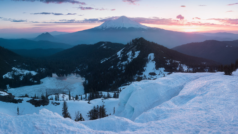 Elevated view of Heart Lake and Castle Peak, covered in snow during winter, with Mount Shasta standing tall in the background during sunrise
