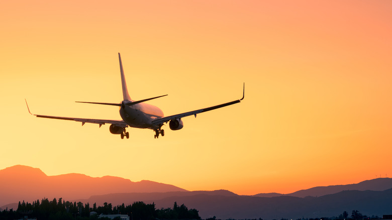 Unmarked airline jet making a landing at sunset with mountains in the backgrround.