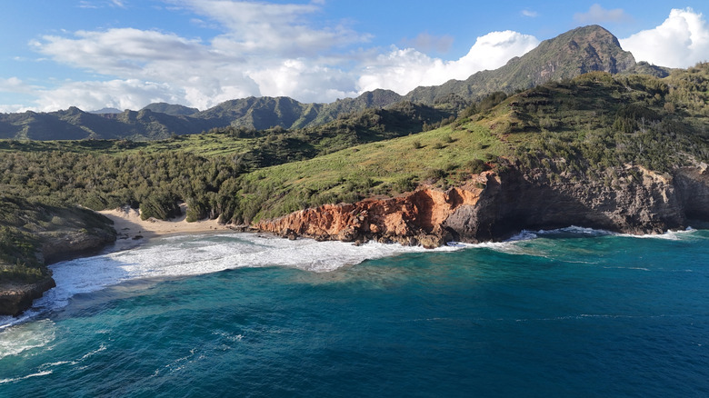 High tide on Kipu Kai beach in Hawaii surrounded by mountains.