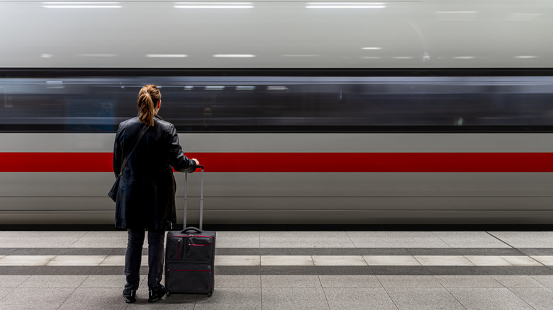 A woman stands on a platform as a high-speed train arrives