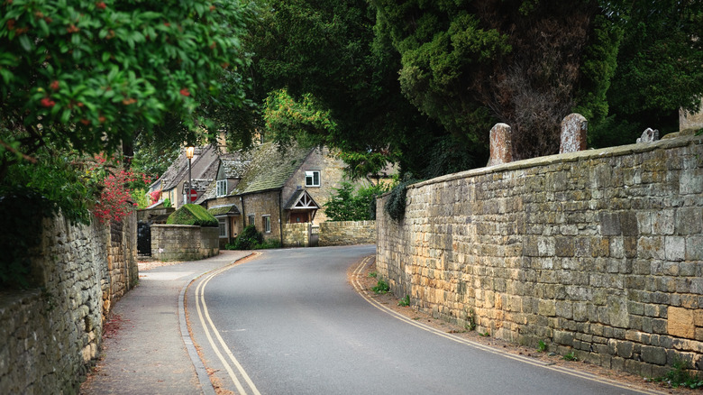 Road with stone walls, under trees, leading into English village