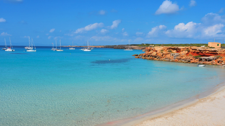 Panoramic view of Cala Saona with sandy beach, and rocky coast and boats in the distance