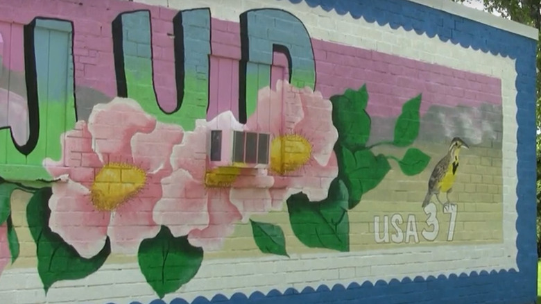 A mural of a stamp with pink flowers, a yellow bird, and 'JUD' on a wall