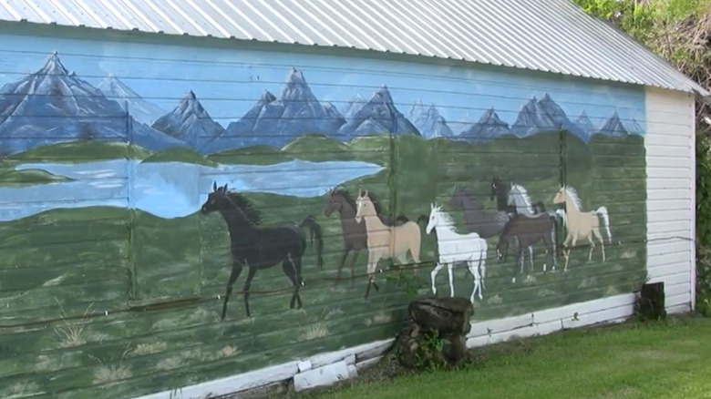 A mural of horses running through a prairie with a lake and mountains in the background