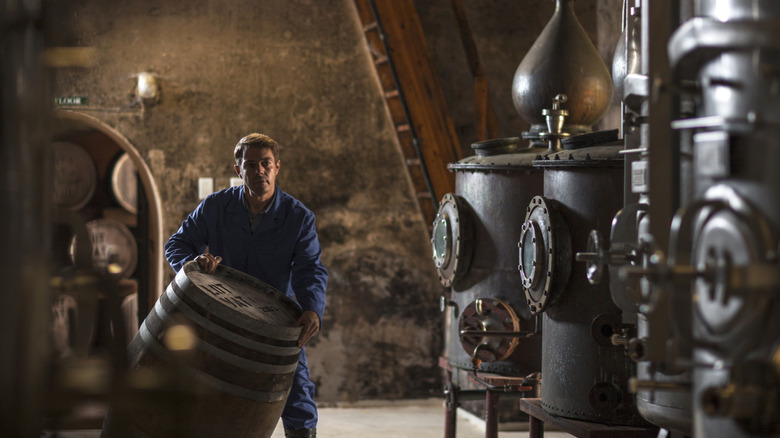 A man moves a barrel in a basement distillery