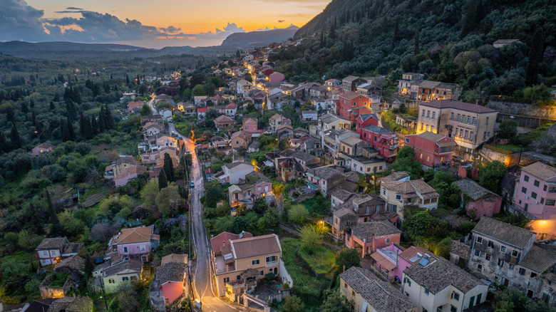 Village houses lit up surrounded by trees at sunset