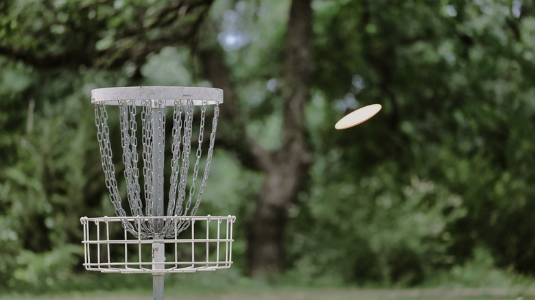 A frisbee flies towards disc golf basket