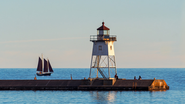 Grand Marais Lighthouse in Minnesota with a sailboat in the background on Lake Superior