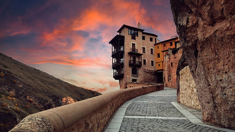 Pavement snaking toward houses hanging over the cliffside against sunset in Cuenca Spain