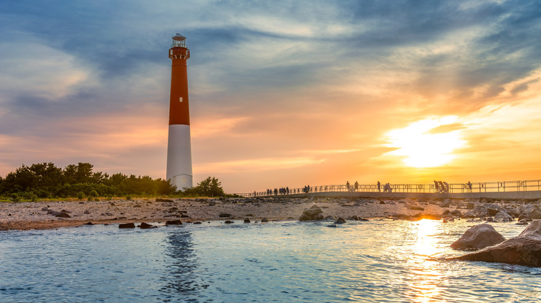 Barnegat Lighthouse rises over visitors on a walkway as the sun sets in the background on the New Jersey coast